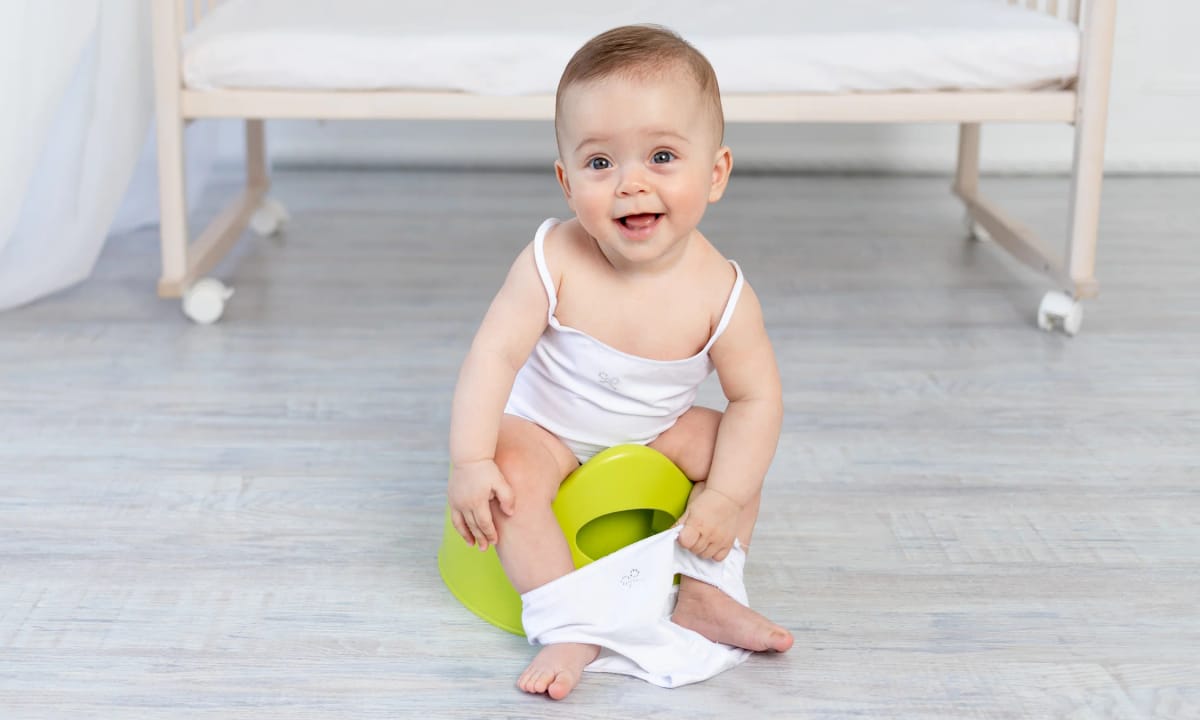 Smiley baby sitting on a green potty doing elimination communication