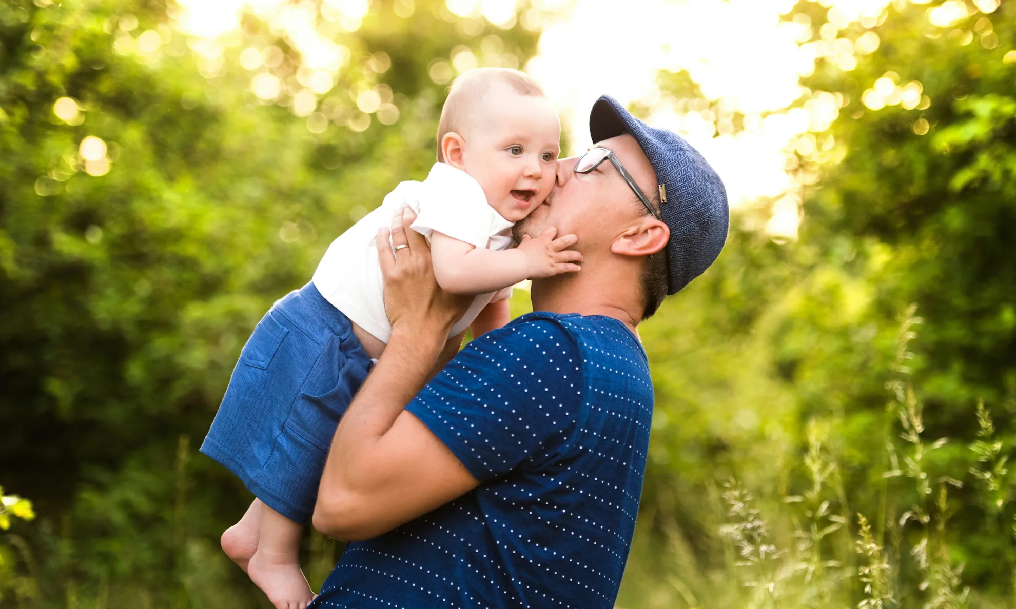 Father holding baby up infront of lush green woodland